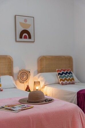 A hotel room with two beds, a wall-mounted artwork, a decorative mirror, and a magazine on the bed.