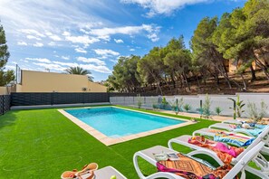 A swimming pool with a surrounding grassy area and lounge chairs.