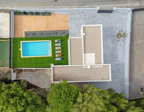 An aerial view of a residential property with a swimming pool, a grassy lawn, and a patio area with lounge chairs.