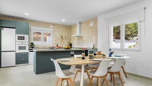 Cozinha moderna com área de refeições, apresentando uma ilha central, armários brancos e vista para o exterior através de grandes janelas.