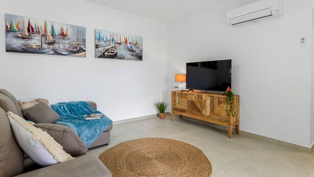 Een woonkamer met een bank, een televisie op een houten kast en twee schilderijen aan de muur.