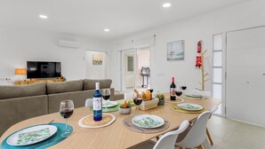 Uma sala de estar moderna com uma TV de tela plana, um sofá e uma área de jantar com mesa posta para refeição.