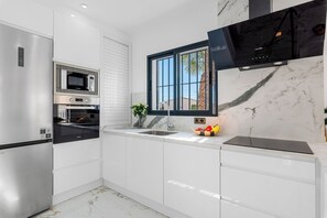 A modern kitchen with white cabinetry, a stainless steel refrigerator, a built-in oven, a microwave, and a black range hood.
