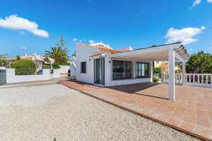 A modern house with a covered patio, a gravel driveway, and a white exterior.