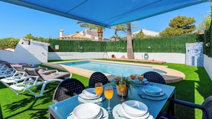 Un espace piscine extérieur avec une table dressée pour les repas, entouré de chaises longues.