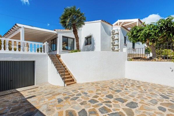 A white building with a stone patio, a staircase, and a palm tree.
