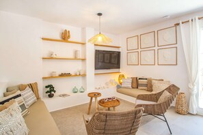 A modern living room with a sofa, a wicker chair, a coffee table, and a TV mounted on the wall.