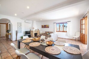 A spacious living area with a dining table set for a meal, a fireplace, and a large window with curtains.