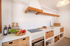 A kitchen with white cabinetry, a wooden ceiling beam, a built-in oven, and a hanging light fixture.