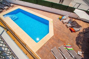 A rectangular swimming pool with a tiled edge, surrounded by lounge chairs and umbrellas.