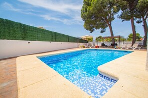 A swimming pool with a tiled edge, surrounded by lounge chairs and a pergola.