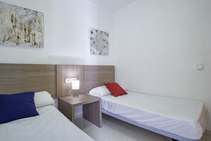 A hotel room with two beds, a nightstand, a lamp, and two wall-mounted artworks. - Apartamento Lynapic - Plusholidays (Calpe)