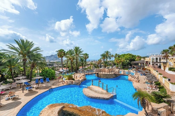Un espace piscine dans un complexe hôtelier, comprenant plusieurs piscines, des palmiers et des chaises longues.