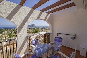 Un balcon avec une table et des chaises en verre, une vue sur le paysage urbain et une montagne à l’horizon.