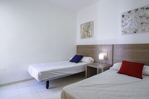 Quarto de hotel com duas camas, uma mesinha de cabeceira, uma luminária na parede e duas obras de arte na parede.