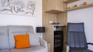 A modern living room with a grey sofa, an orange pillow, a black floor lamp, a black chair, and a wooden cabinet with a blue bowl on top. - Apartamento Lynapic - Plusholidays (Calpe)