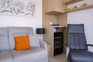 Uma sala de estar moderna com um sofá cinzento, uma almofada laranja, um abajur preto, uma cadeira preta e um armário de madeira com uma tigela azul em cima.