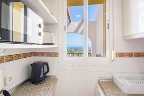 A kitchen with a view of the sea, a kettle, and a microwave. - Apartamento Lynapic - Plusholidays (Calpe)