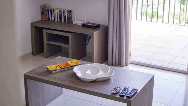 A room with a TV mounted on the wall, a small wooden table with a white bowl and remote controls, and a balcony with a view. - Apartamento Lynapic - Plusholidays (Calpe)