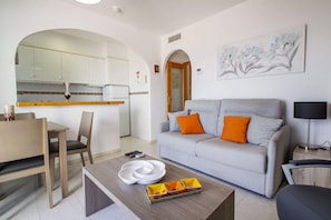 Un salon moderne avec un canapé gris, une table basse et un coin repas comprenant un buffet blanc et un vase.