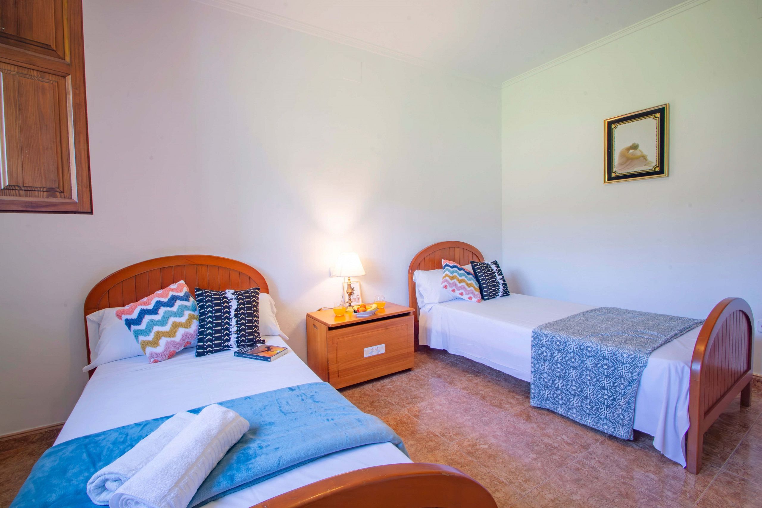 A hotel room with two single beds, a wooden headboard, a nightstand with a lamp, and a framed picture on the wall.