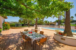 Un espace extérieur aménagé pour les repas, avec une piscine en arrière-plan.