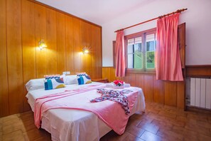 Une chambre d’hôtel avec un mur lambrissé en bois, un lit avec de nombreux oreillers, une fenêtre avec des rideaux et un luminaire fixé au mur.