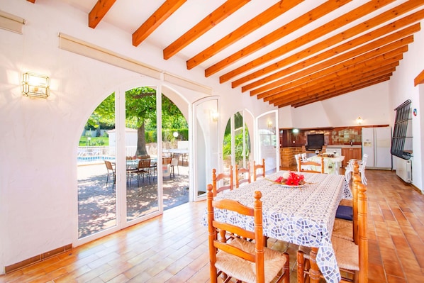 A spacious dining area with a long wooden table, surrounded by chairs, and a kitchen area with a tiled backsplash and modern appliances.