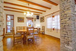 A dining area with a wooden table and chairs, a chandelier, stone walls, and a clock on the wall.