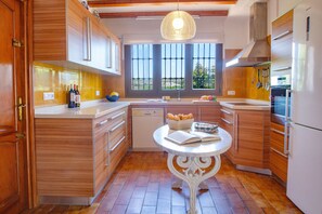 Une cuisine moderne avec des meubles en bois, un plan de travail blanc, un lave-vaisselle encastré et une fenêtre donnant sur un paysage verdoyant.