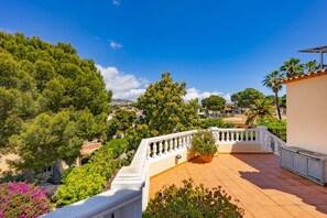 A terrace with a white balustrade, potted plants, and a view of a residential area with trees and houses.