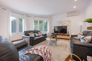 A modern living room with leather sofas, a flat-screen TV, and a large window with curtains.