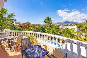 A terrace with a table set for two, chairs, and a view of a mountainous landscape.