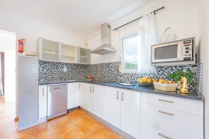 A modern kitchen with white cabinets, a stainless steel dishwasher, a microwave, and a tiled backsplash. - Villa Duke - Plusholidays (Calpe)