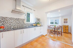 A kitchen with white cabinets, a tiled backsplash, a microwave, and a dining area with a table and chairs.