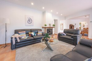 A living room with a sofa, armchair, and glass coffee table. There is a fireplace and a dining area visible in the background. - Villa Duke - Plusholidays (Calpe)