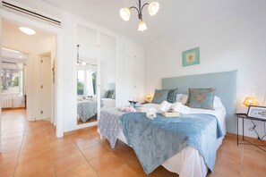 A bedroom with a large bed, a bedside table, a mirror, and a view of the outside.
