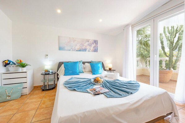 A hotel room with a bed, a bedside table, a lamp, a window with a view of a cactus, and a wall-mounted painting.