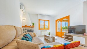 Una sala de estar con un sofá color beige, una mesa de centro de madera, un televisor y una ventana con persianas anaranjadas.