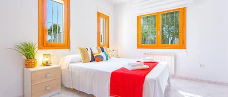 Un dormitorio con cama, mesitas de noche y ventanas.