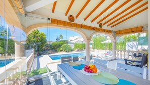 Zona de piscina con mesa lista para comer, vista a la piscina y un área de estar cubierta.