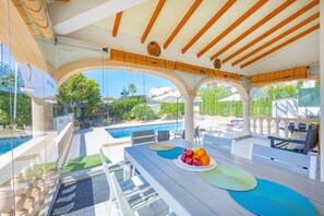Ein Poolbereich mit Esstisch, Blick auf den Pool und einer überdachten Sitzgelegenheit.