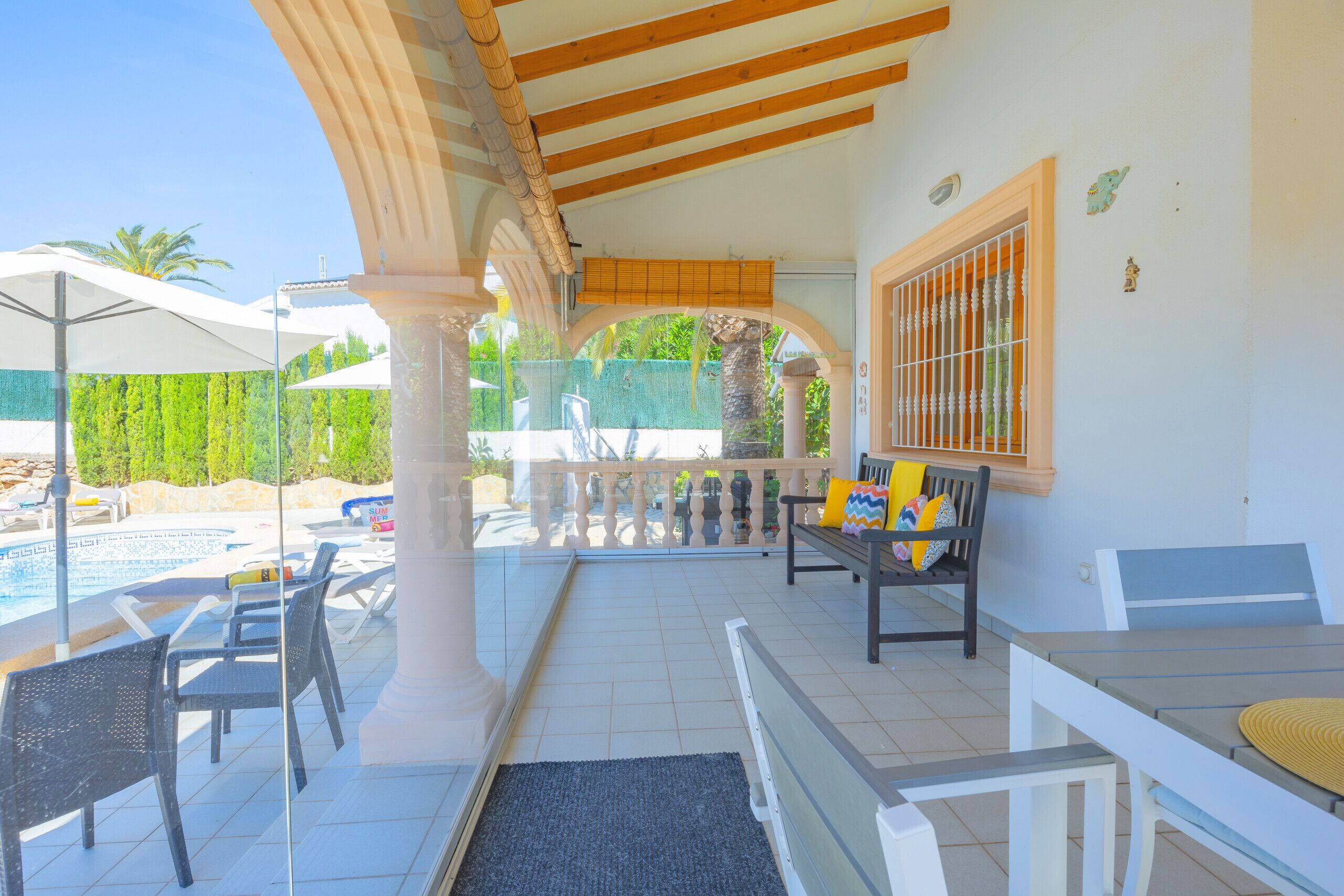 A covered outdoor seating area with a pool, chairs, and a table.