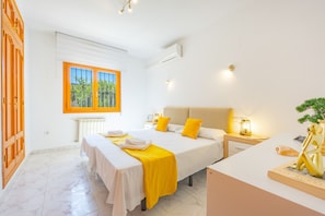 A hotel room with a large bed, a desk, a chair, a window with a view of greenery, and a small table with a lamp. - Villa Mona - PlusHolidays (Calpe)