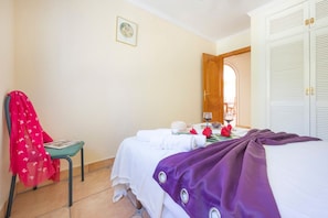 A hotel room with a bed, a chair, a table with towels and a wine glass, and a door leading to another room. - Villa Ursula - Plusholidays (Calpe)