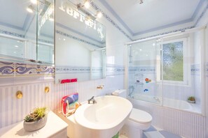 Un bagno con un lavandino ampio e bianco, un WC e una vasca da bagno. Si vede del verde attraverso una finestra.