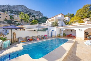 A swimming pool with lounge chairs, a barbecue area, and a view of a mountainous landscape.