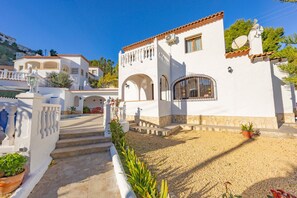 A white building with a tiled roof, a balcony, and a gravel driveway.