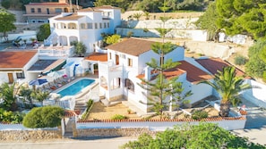 A multi-story villa with a swimming pool, outdoor seating, and a stone wall.