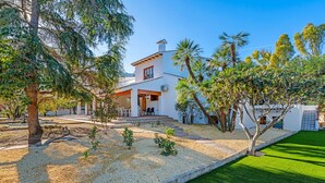 Una casa a due piani con un patio, circondata da alberi e un prato curato.
